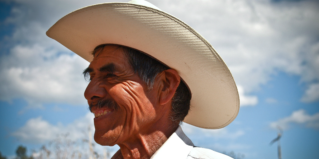 A Mexican man in a cowboy hat smiling, and looking into the distance.