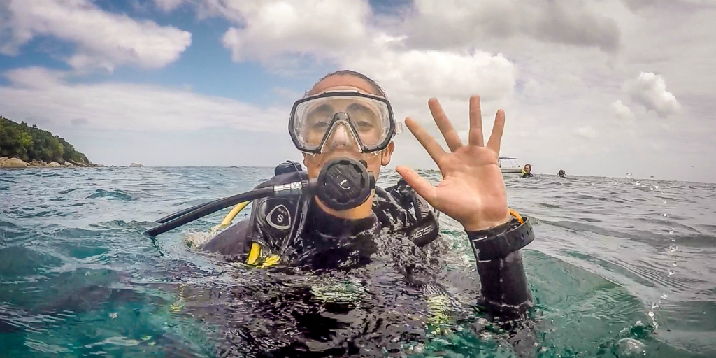 A dive training student waving from the water in full diving gear.
